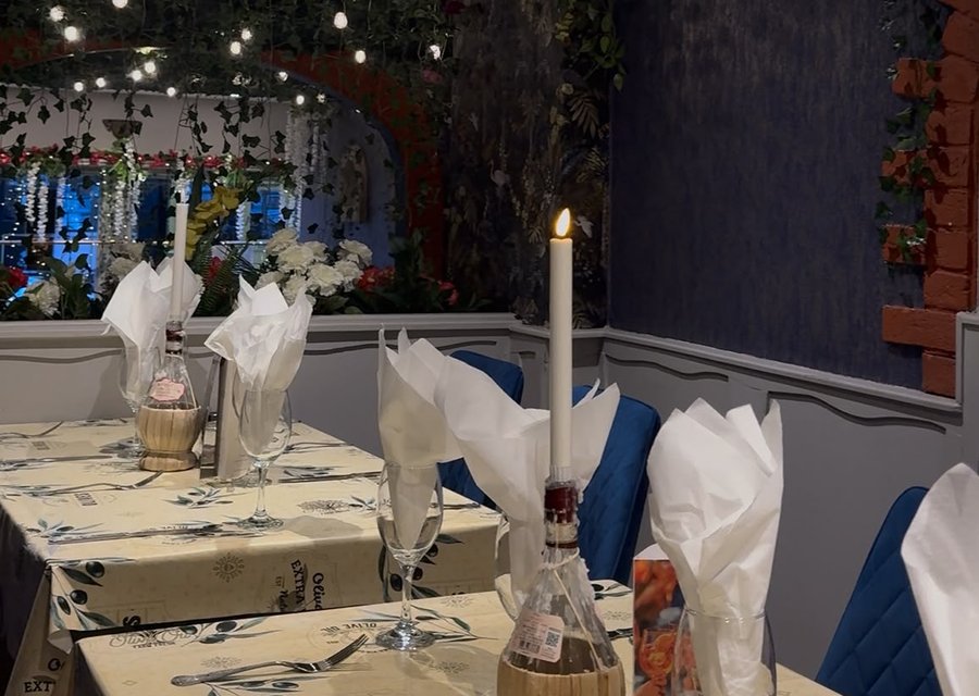 Candlelit tables laid with wine bottles and napkins in the San Marcos dining room, fairy lights and greenery behind