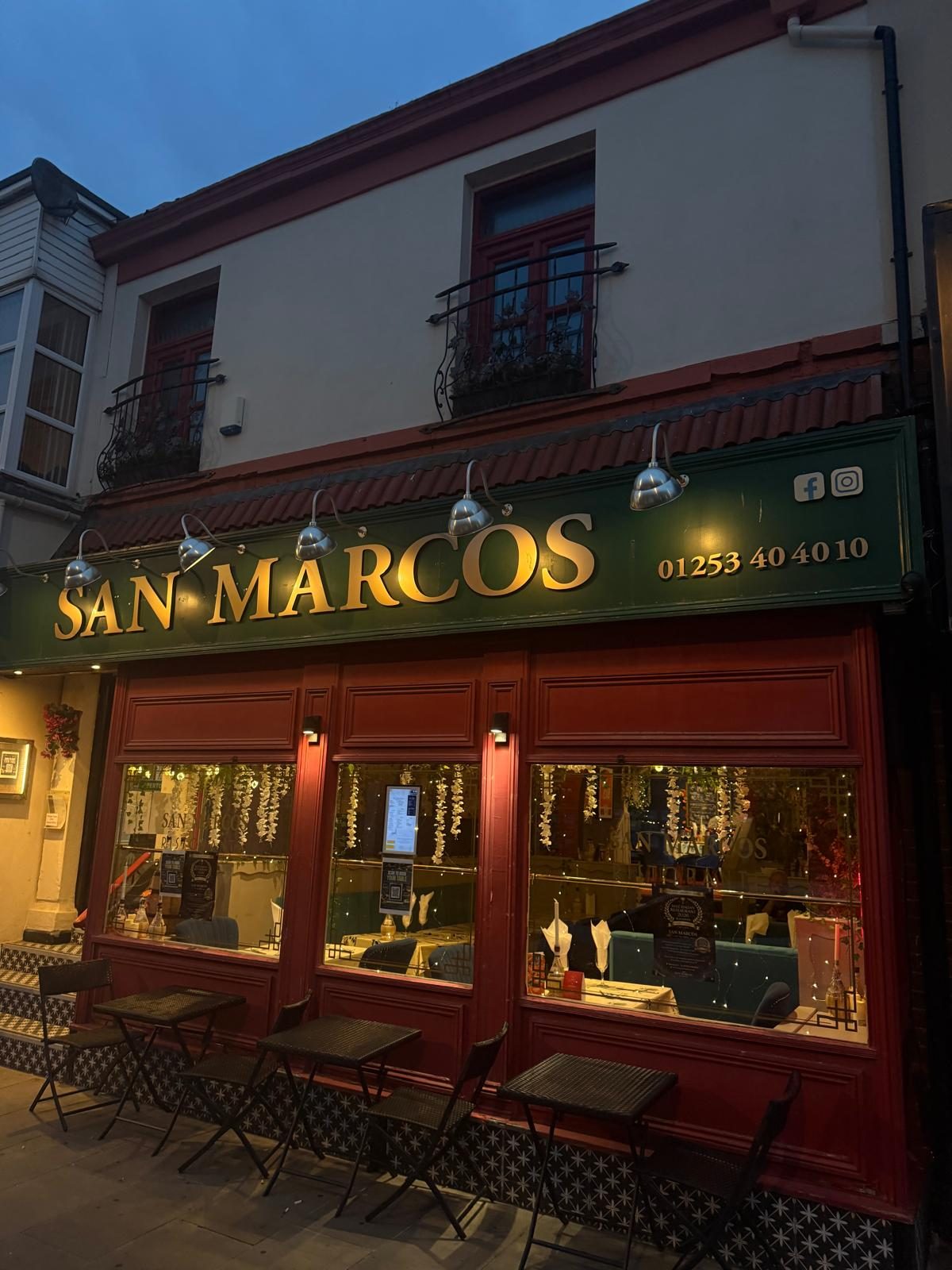 The San Marcos shopfront at dusk — gold lettering on green above glowing red-framed windows